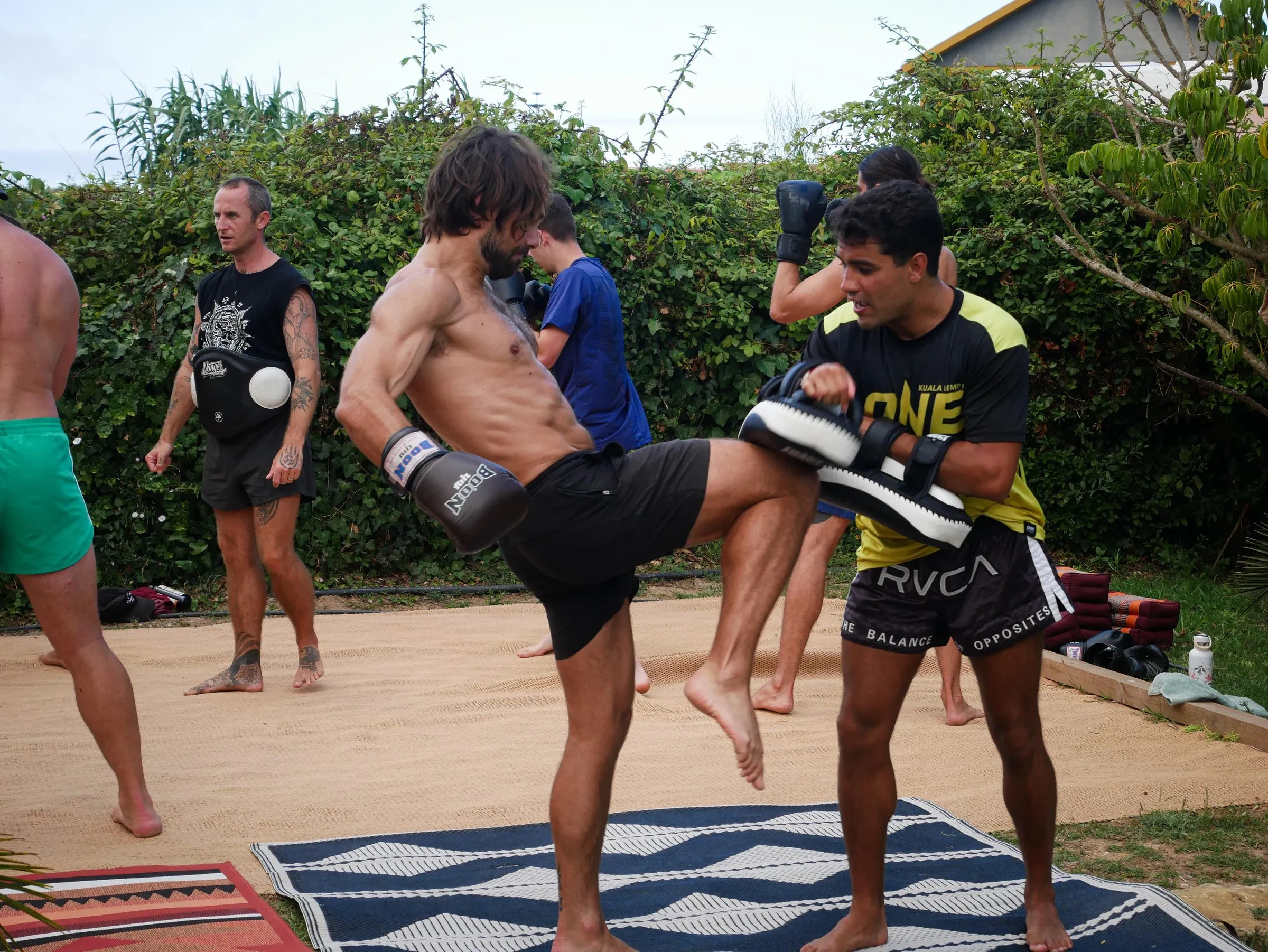 Rui Botelho holding pads outdoors while a client throws a knee during a private session